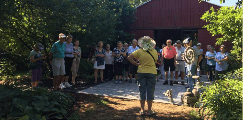 Person speaks to a group outside surrounded by trees and a barn.