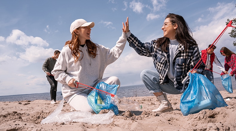 Two women high five while picking up trash at a volunteer event, demonstrating the positive impact of effective volunteer management.